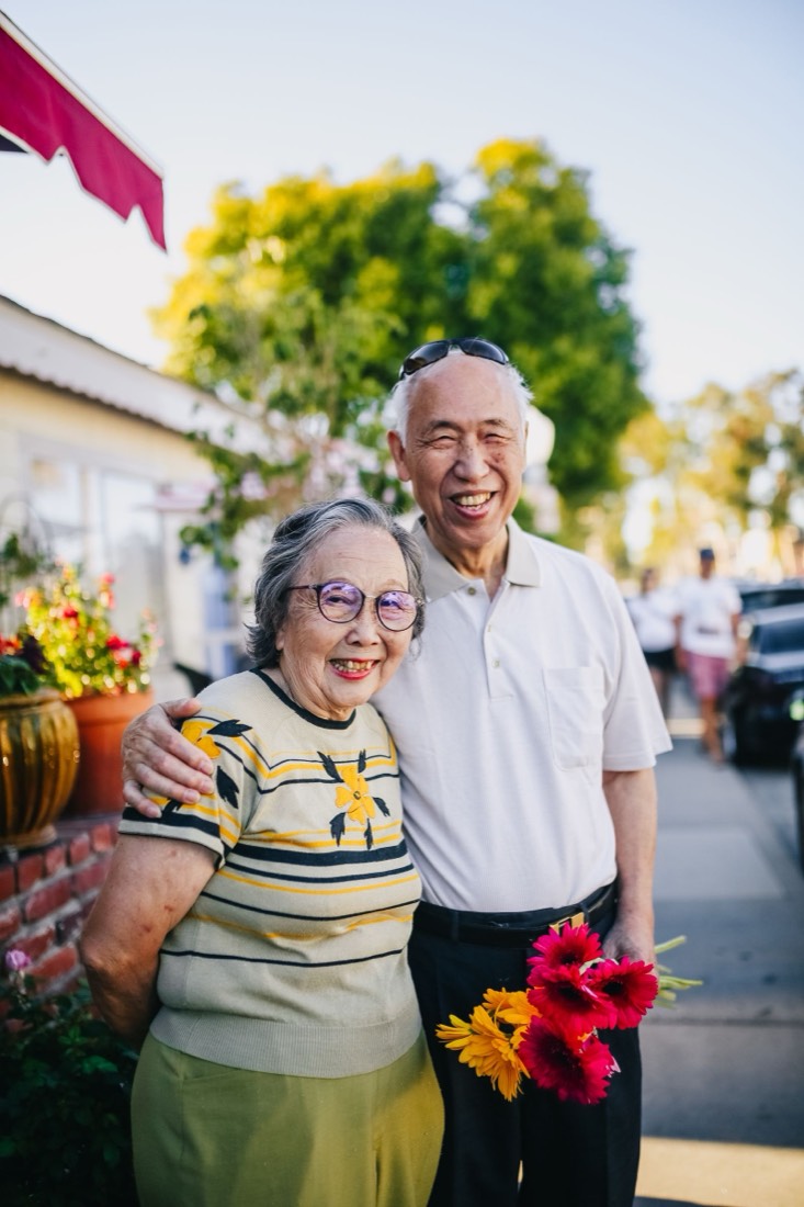 An older couple smiling together outdoors, holding fresh flowers